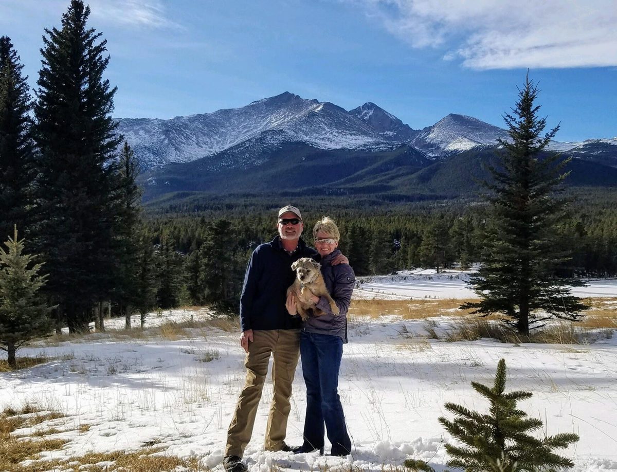 Hillary Davies and Greg Walter standing in a snowy mountain meadow, holding a small terrier